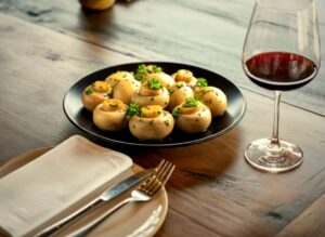 Plato de setas en mesa de restaurante con copa de vino tinto, maridaje para cocina de otoño.