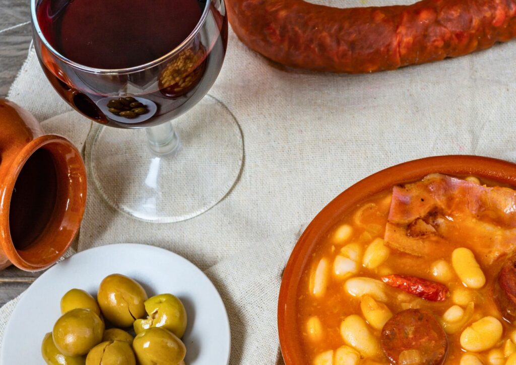 Copa de vino tinto junto a un plato de alubias con chorizo y caldo tradicional, comida de invierno ideal para maridar en restaurantes de Valencia.