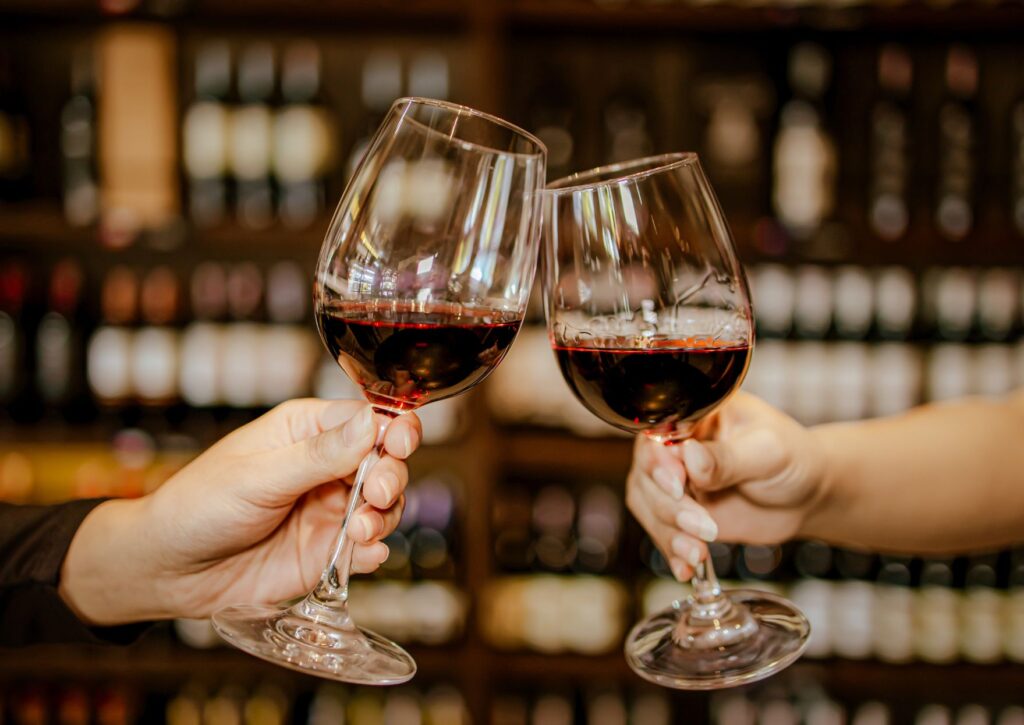 Brindis con dos copas de vino tinto en un restaurante, con estantería de botellas al fondo, ideal para una cena de San Valentín en Valencia.