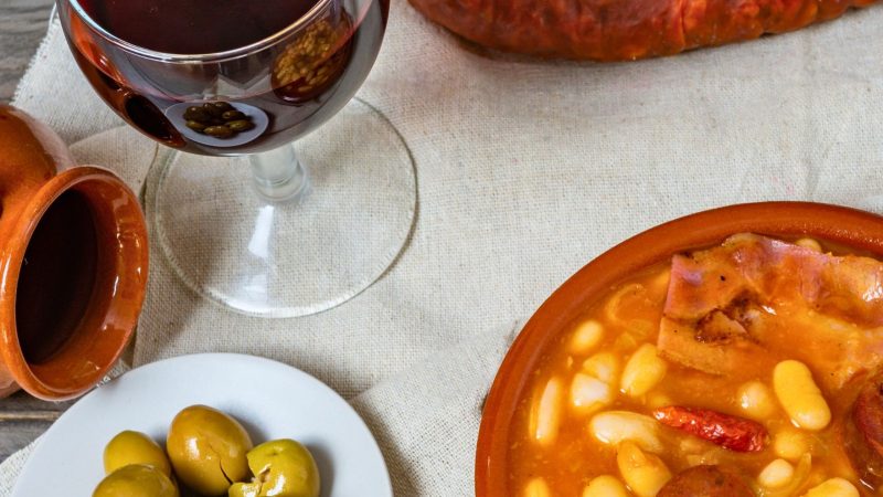 Copa de vino tinto junto a un plato de alubias con chorizo y caldo tradicional, comida de invierno ideal para maridar en restaurantes de Valencia.