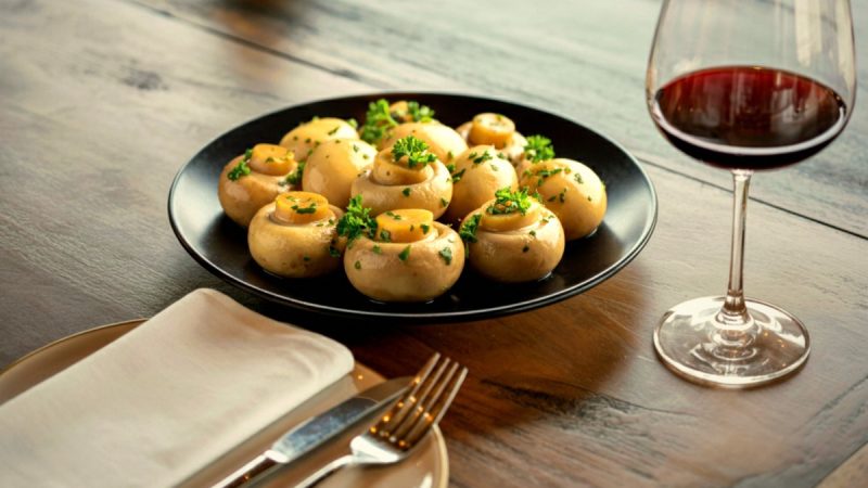 Plato de setas en mesa de restaurante con copa de vino tinto, maridaje para cocina de otoño.